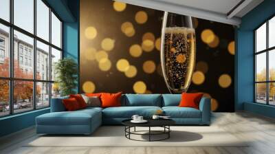 A champagne glass with golden bubbles is lifted at a celebration with a festive backdrop. Wall mural