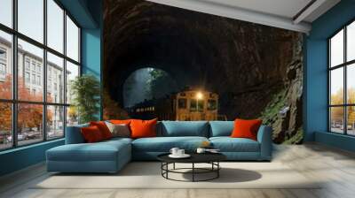 A train enters an old mining tunnel with light streaming from the end. Wall mural