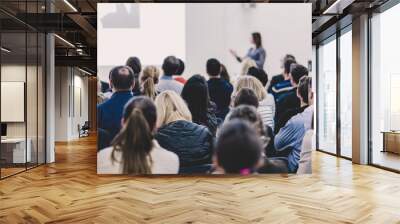 Business and entrepreneurship symposium. Female speaker giving a talk at business meeting. Audience in conference hall. Rear view of unrecognized participant in audience. Copy space on whitescreen. Wall mural