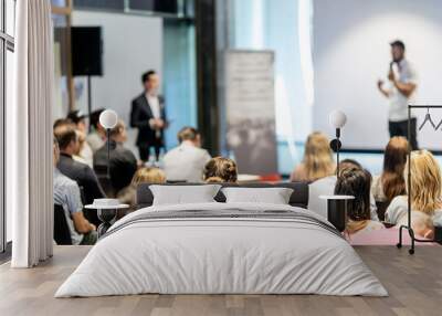 Business and entrepreneurship symposium. Speaker giving a talk at business meeting. Audience in conference hall. Rear view of unrecognized participant in audience. Wall mural