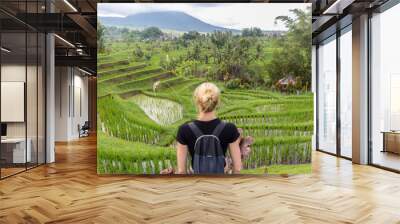 Casual caucasian female tourist wearing small backpack looking at beautiful green rice fields and terraces of Jatiluwih on Bali island, Indonesia. Wall mural