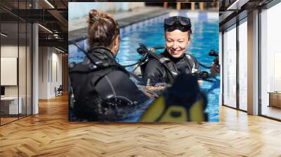 Female diving instructor teaches student to scuba dive in swimming pool. Lady getting first experience with scuba diving under the guidance of experienced recreational diving instructor on vacation. Wall mural