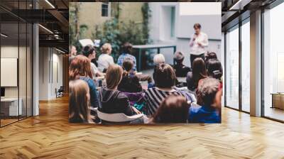 Female speaker giving presentation in lecture hall at university workshop. Audience in the conference hall. Rear view of unrecognized participant in audience. Scientific conference event. Wall mural