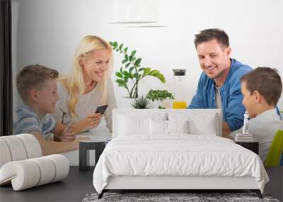 Happy young family playing card game at dining table at bright modern home. Spending quality leisure time with children and family concept. Cards are generic and debranded. Wall mural