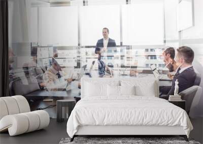 Successful team leader and business owner leading informal in-house business meeting. Business people working on laptops in foreground and glass reflections. Business and entrepreneurship concept. Wall mural