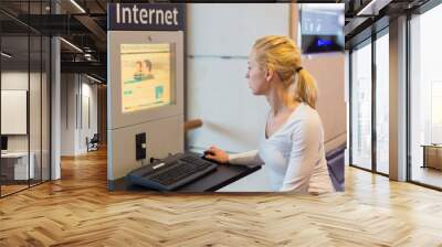 Young caucasian woman using comupter with public internet access point on airport. Wall mural