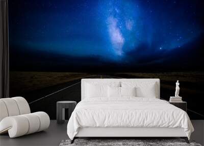 A highway disappearing into the distance illuminated by a star filled dramatic night sky in a rural landscape Wall mural