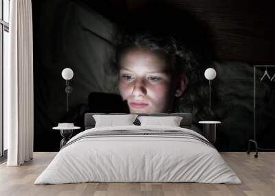 close up of a teenage girls face lying on a pillow in bed lit up by the light from a cellphone Wall mural