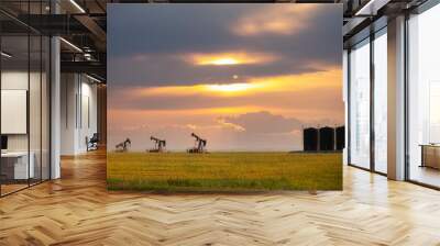 Three crude oil pump jacks and storage tanks in a canola field in a summer countryside landscape Wall mural