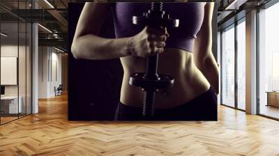 Slim athletic woman Holding dumbbell in the hand on black Wall mural