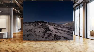 A man standing far away on a tall mountain under the starry dark blue sky with snow glimmering under the moonlight. Wall mural