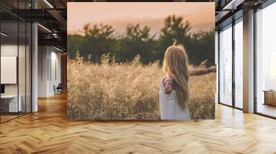 girl with open hands enjoying rural magic atmosphere among golden fields in the countryside Wall mural