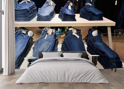 An assortment of jeans is carefully stacked on a shelf in a clothing store. Wall mural