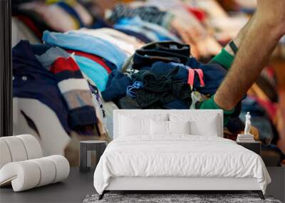 Person sorting second hand clothes by size and gender Wall mural