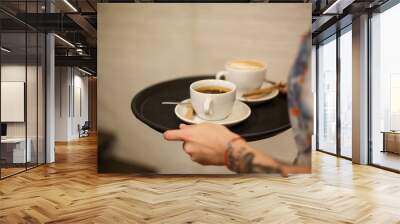 Woman bring two white cups of latte and americano coffe on tray Wall mural