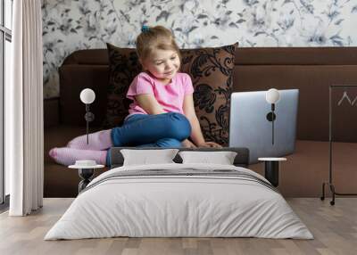 A first grader girl studies at home on distance learning using a laptop. Children education concept. Wall mural