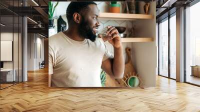 African American attractive male drinking a pure water, follow healthy lifestyle. Handsome guy feel thirsty, drink daily amount of pure liquid, standing at kitchen, healthcare concept Wall mural