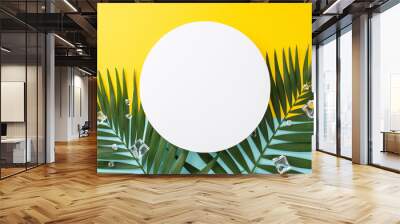 Chill out and enjoy the summer vibe with a top view flat lay of green palm leaves and ice cubes on blue and yellow background. Ideal for vacation concept with empty circle for text or branding Wall mural