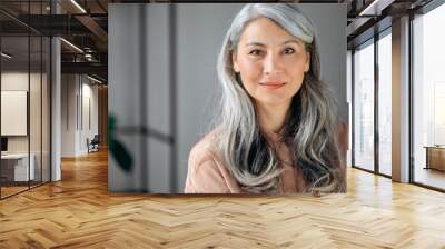 Close-up portrait of beautiful influential confident mature gray-haired Asian woman ceo, lawyer, real estate agent, stands in the office, dressed in stylish clothes, looks at camera, friendly smiling Wall mural