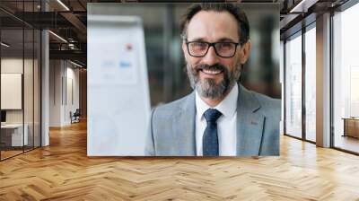 Close-up portrait of mature bearded businessman dressed in stylish suit and eyeglasses, looking at the camera with friendly smiling, standing in the office Wall mural