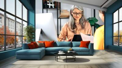 Friendly female mature hr manager listening and looks a resume of a new applicant introduction for a job. Gray-haired female employer talks and meets with female job seeker. Wall mural