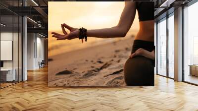 Meditating girl on the seashore during sunset. She is sitting in a lotus position. Close-up photo Wall mural