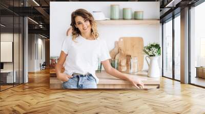 Portrait of a charming young blonde girl with blue eyes and in a white t-shirt who poses in the kitchen and smiling Wall mural