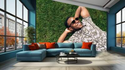 Portrait of a handsome young smiling african american man whos resting  on a grass in nature during a warm summer day. Top view. Copy space Wall mural