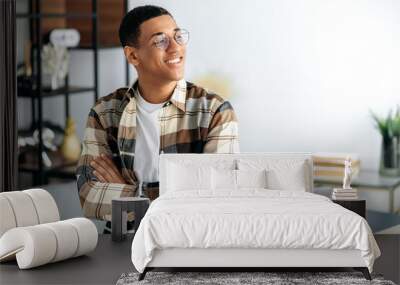 Portrait of an attractive confident positive young mixed race latino man with glasses, designer or freelancer, stylishly casual dressed, stand near a desk with arms crossed, looking to the side, smile Wall mural