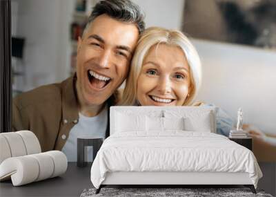 Portrait of beautiful cheerful marriage mature couple in casual clothes, Caucasian husband and wife taking selfie on smartphone, having fun together, looking at camera, smiling Wall mural