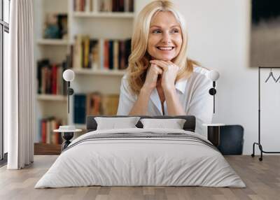 Portrait of happy elegant successful mature blonde woman in white stylish shirt, sits at the desk at office, taking a break from work, looking to the side, thinking, smiling friendly Wall mural