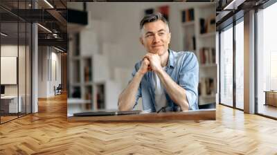 Portrait of happy handsome mature gray-haired caucasian freelancer or manager, stylishly dressed, sitting at the table, taking a break from work, dreaming about vacation, looking away, hands joining Wall mural