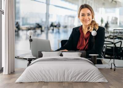 Successful confident caucasian business woman dressed in elegant wear, executive, recruitment, product manager, sits in a modern office, works in a laptop, looks at camera, smiling friendly Wall mural