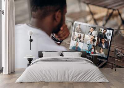 Video call. Video conference. Successful African American freelancer communicate by a video conference with his colleagues using a laptop while sitting in cafe in a summer terrace Wall mural