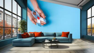 the blue ribbon awareness with red blood drop in woman hands isolated on a blue background. World diabetes day,14 november. Copy space. Top view Wall mural