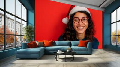 beautiful smiling young woman wearing santa hat on red background Wall mural