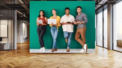 We cant function without our connections. Portrait of a group of young designers using digital devices while standing together against a green background. Wall mural