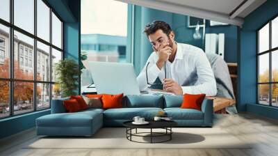 Hes finding it tough to stay focused. Shot of a young businessman looking stressed out while working on a laptop in an office. Wall mural