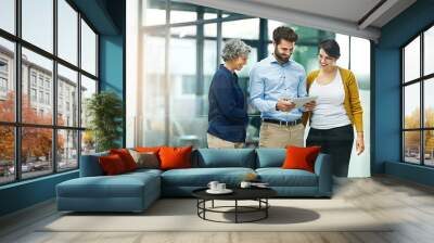 The never get tired of the office tablet. Shot of a group of creative businesspeople looking at a tablet together in the office. Wall mural