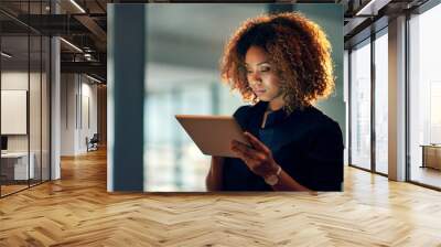 Working smart, working hard. Shot of a young businesswoman using a digital tablet during a late night at work. Wall mural