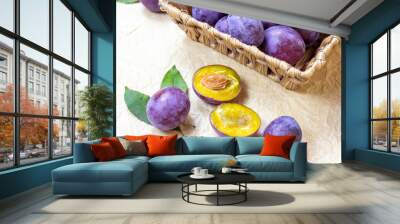 Fresh raw blue and violet plums in wooden bowl with green leaves on light paper background. Wall mural