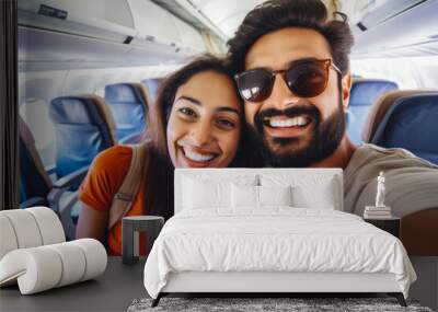 Happy indian tourist couple taking a selfie inside an airplane. Positive young couple on a vacation taking a selfie in a plane before takeoff. Wall mural