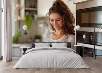 beautiful happy girl with a smile on her face stands in her modern kitchen and holds a smartphone in her hands Wall mural