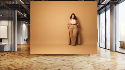 Plus size model posing on a beige background in stylish and modern clothes Wall mural