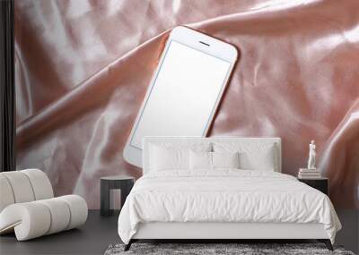 Flat lay concept of feminine light background with mobile phone on pink silk with copy space. Wall mural