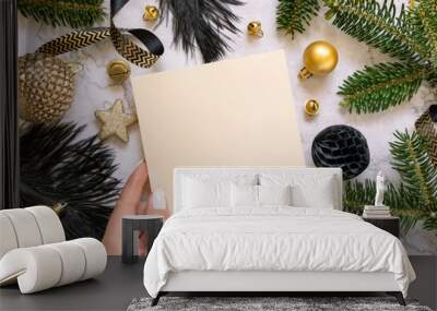 Hand holding Card near black and golden Christmas decorations and fir branches, Mockup Wall mural