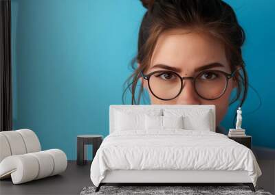 An attractive young female scientist wearing glasses, looking directly at the camera with her hair tied back in a bun, against a blue background Wall mural