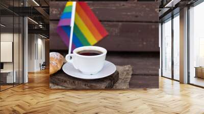 A cup of coffee and a croissant on a wooden table against the background of the LGBT flag Wall mural