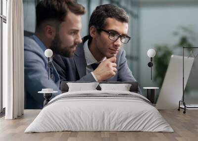 Two young businessmen sitting at workplace and working together in office Wall mural