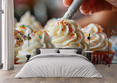 A close-up of a baker's hand piping frosting onto cupcakes, topped with colorful sprinkles, showcasing intricate detailing. Wall mural